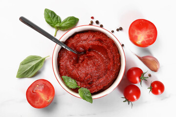 Tasty tomato paste in bowl and ingredients on white table, flat lay