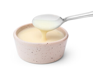 Condensed milk flowing down from spoon into bowl isolated on white