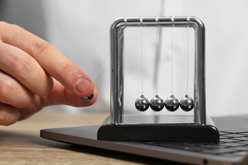 Man playing with Newton's cradle and laptop on wooden table, closeup. Physics law of energy conservation