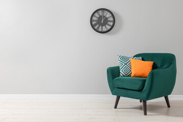 Comfortable armchair with cushions near light grey wall indoors. Space for text