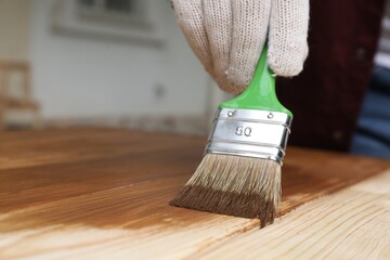 Man applying wood stain onto wooden surface against blurred background, closeup. Space for text