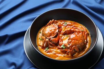 Delicious boiled crabs with sauce in bowl on blue tablecloth. Space for text