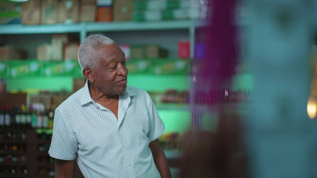 One black senior shopping for drinks at supermarket. African American elderly person staring at alcoholic aisle, picking product from shelf