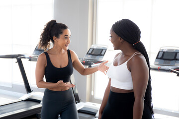 Two young woman talking in the gym, woman in sportswear and friend or coach relax and discussing...