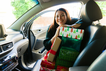 Beautiful hispanic woman in the car with a lot of christmas presents - obrazy, fototapety, plakaty