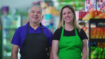 Portrait of two happy employees of supermarket business with smiling expressions. A senior caucasian male staff manager next to a middle-aged female worker wearing aprons, job occupation concept.