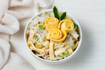 Salad of shredded boiled chicken, fresh cucumber, onion and chopped egg pancakes closeup in bowl on table. Decorated with roses from egg pancakes, Party dinner. Top view from above