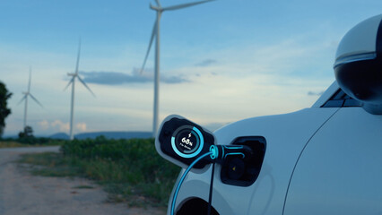 Electric car recharging energy from EV charging station display futuristic smart battery status hologram by EV charger plug cable in wind turbine farm. Alternative clean energy sustainability. Peruse