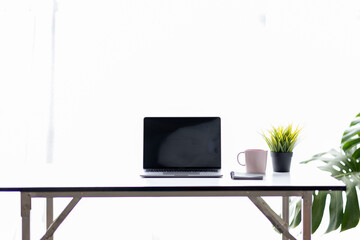 Laptop Computer, notebook, and eyeglasses sitting on a desk in a large open plan office space after...