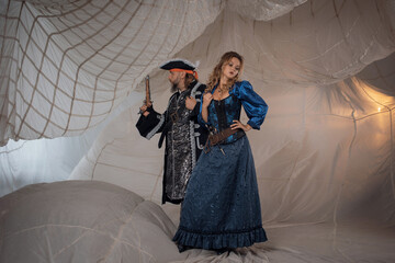 A lady and a pirate in an antique doublet and hat, a couple in pirate costumes. sails on the background - 673012789