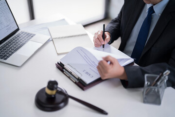 Male lawyer reading and checking financial document of business to analysis about legal agreement and terms of business contract while working on the desk with laptop technology in law firm