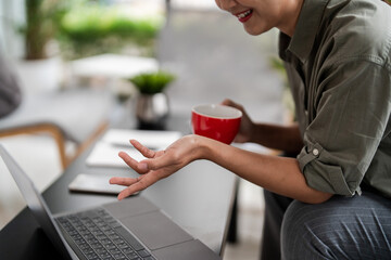 Asian casual businesswomen sit on couch to drinking coffee and meeting with colleague on video call