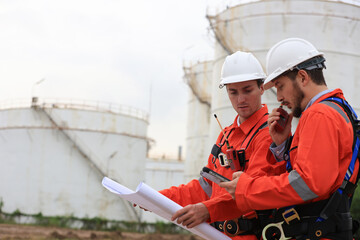 Team Engineers wearing safety harnesses working and discussing with blueprint at the Oil Refinery...