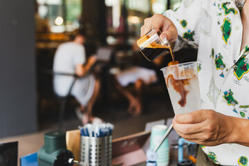 Barista pouring coffee into glass amnking iced coffee for customer.