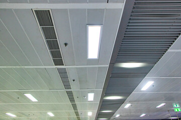 Ceiling with light bulbs lighting with ventilation pipes in train station in Thailand. Ceiling is...