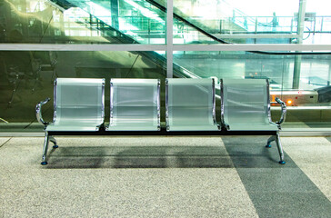 Stainless steel chairs for passengers waiting for their bus at train station in Thailand. Luster reflected from stainless steel chair. Background is mirror and escalator. Modern design to serve public - obrazy, fototapety, plakaty