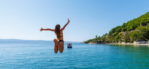 Happy young female jumping into water- vacation, freedom, travel destination concept - obrazy, fototapety, plakaty