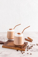 Two chic glasses with cappuccino coffee or cinnamon latte a delicious with eco straw on a wooden cutting board. Front vertical view. A copy space.