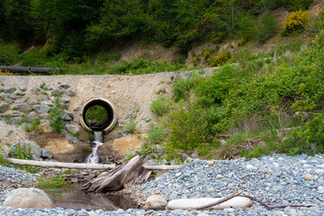 An image of a large concrete culvert running under a rural road way and diverting waste water runoff.