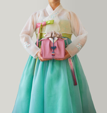 The woman wearing colorful Hanbok, Korean traditional dress. Holding a gift wrapped in silk(bojagi) in her hand. Isolated on white background. Holiday greeting concept. 
