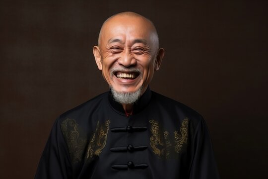 Portrait of a senior asian priest laughing against dark background.