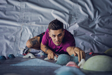 Fototapeta premium A strong male climber climbs an artificial wall with colorful grips and ropes.