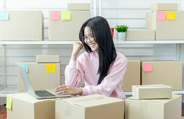 Happy young Asian woman entrepreneur. Using laptop computer checking product purchase order and preparing parcel for delivery to customers. Selling products online. Online Shopping. Online business