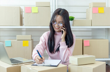 Young asian woman talking on smartphone and checking product purchase order and preparing parcel for delivery to customers. Selling products online. Online Shopping. Online business