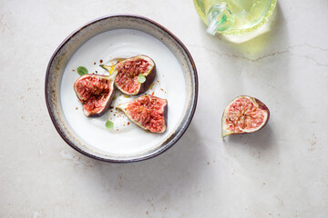 Bowl of yogurt with fresh torn figs on a light-beige stone background, horizontal shot, top view