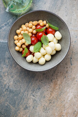 Bowl with scamorza, smoked perlini, cherry tomatoes and basil, top view on a grey and beige granite background, vertical shot with space