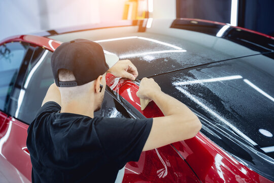 The process of installing protective film on the new red car.