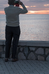 Hombre mayor de espaldas, paseo marítmo de Máaga, anciano haciendo fotos a la playa al amanecer, primeros rayos de sol