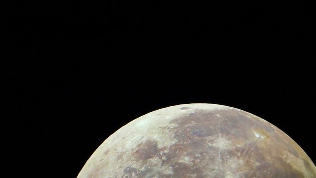 The colored Moon moves in the frame. Real shooting through an astronomical telescope. Natural surface of the Moon with meteorite craters