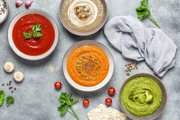 Set of colored soups. Cream of mushroom soup, tomato soup, pumpkin soup and broccoli soup. Healthy food. Gray rustic background. View from above.