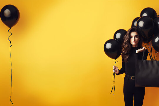 Belle et jeune femme brune habill&eacute;e en noir portant un sac de shopping sur l'&eacute;paule et des ballons baudruches noirs sur un fond jaune moutarde. Shopping, black Friday, Soldes - Espace texte