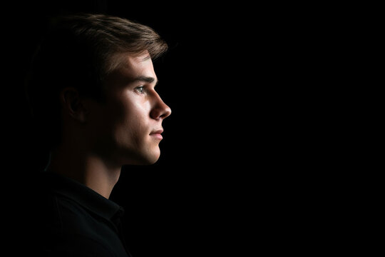 Low Key portrait of a young man against a black background, Dark relaxed profile shot with black copy spac