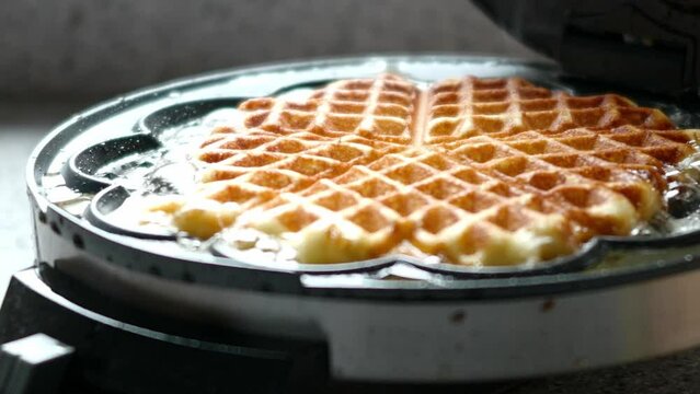 In einem Waffeleisen werden Waffeln in Herzform gebacken.