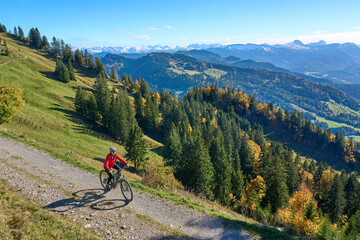 Fototapeta na wymiar pretty senior woman riding her electric mountain bike in autumn and enjoying the spectacular view over the Allgau and Bregenz Forest alps near Steibis, Bavaria, Germany