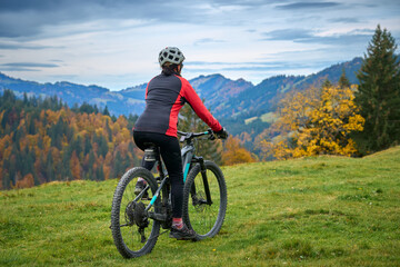 pretty senior woman riding her electric mountain bike in autumn and enjoying the spectacular view...