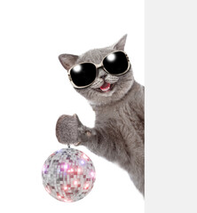Happy cat wearing sunglasses looks from behind empty banner and shows dico ball. isolated on white...