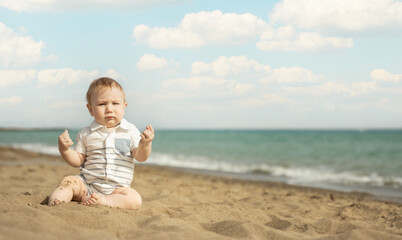 A baby boy sitting on a sand on the seaside