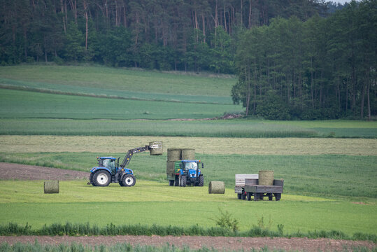 Ciechanów, Poland - May 22, 2022: Haymaking in the countryside. Tractors with trailers and machines for loading hay bales. Work in the field, agriculture.