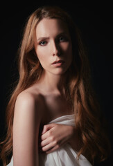 Fototapeta premium Tragic portrait of lovely young sad girl against black background. Sorrowful woman among the dark