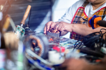 Selective focus to hand of an electric motor repairman. Mechanic is repairing an electric motor by replacing the copper coil. Electric fan motor repair work . - obrazy, fototapety, plakaty