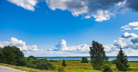Obraz premium Summer landscape with lake, grass, trees against a blue sky with white clouds
