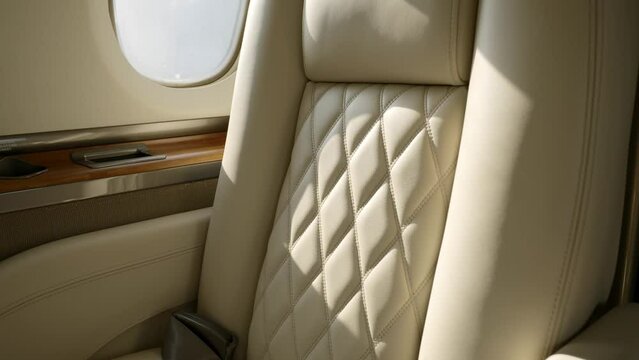 Rotating shot of leather passenger seat lighted by sun beams. Luxury design of upholstery with rhombus relief patterns and wooden inlay of fuselage interior of jet Hawker