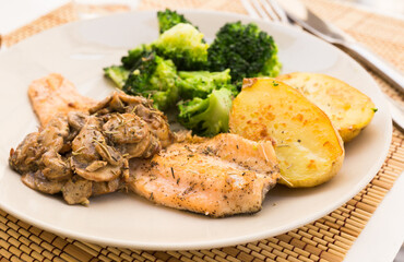 Fried river trout fillet with a complex side dish of broccoli, baked potatoes and mushroom sauce