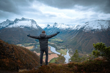 Traveler with his back turned, hands open, enjoying a mountain landscape in the Norwegian fjords of the city of Andalsnes, Norway. - obrazy, fototapety, plakaty