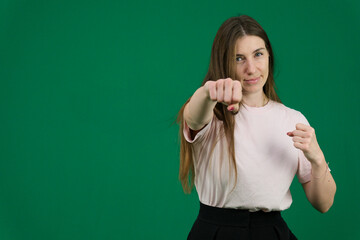 woman punching the air with her fists training at home. emotions of a young girl on a green background chromakey beautiful facial features real people pink T-shirt white skinned European. 