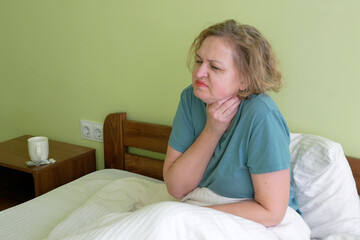 Middle aged woman sit in bed under warm blanket blow running nose using tissue, and coughs,   sick female suffer from influenza or grippe at home